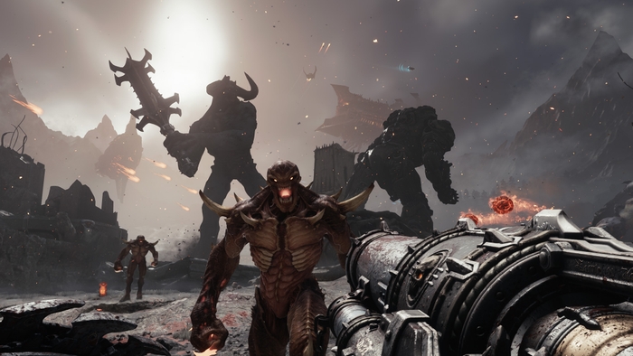 A first-person view of Doom: The Dark Ages gameplay. The player character points a gun at one demon advancing at him as a giant demon and robot battle in the background.