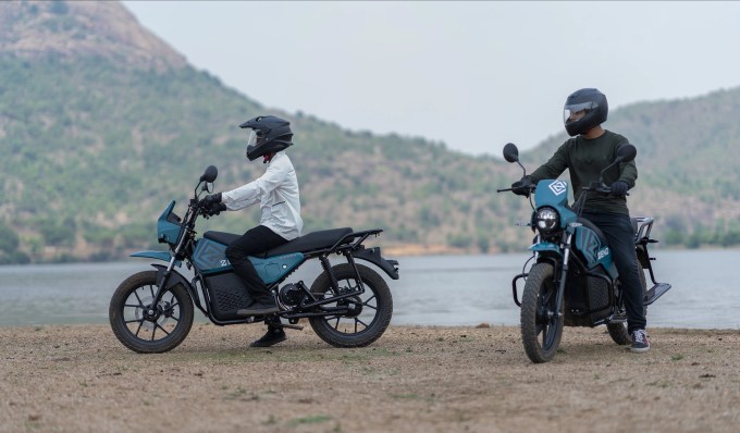 Two motorbikes with riders are parked in front of a lake.